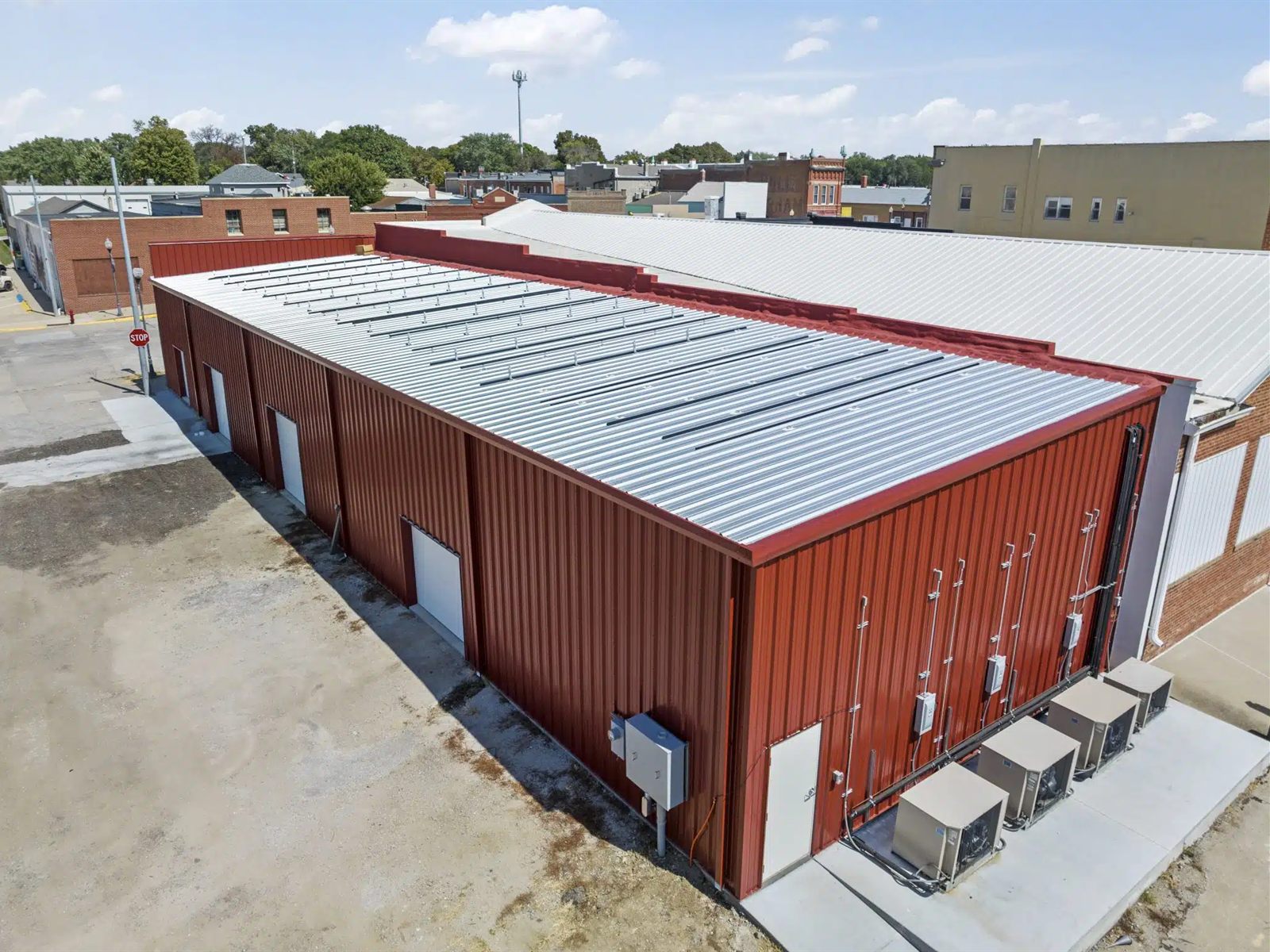Aerial view of a finished steel commercial building with red wall panels, a silver metal roof and white overhead doors