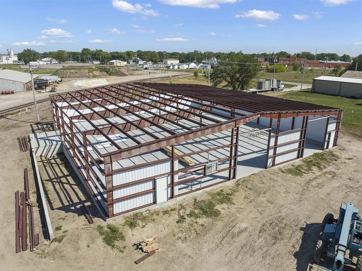 Aerial view of a red iron steel frame under construction, with white wall panels going on and steel members on the ground