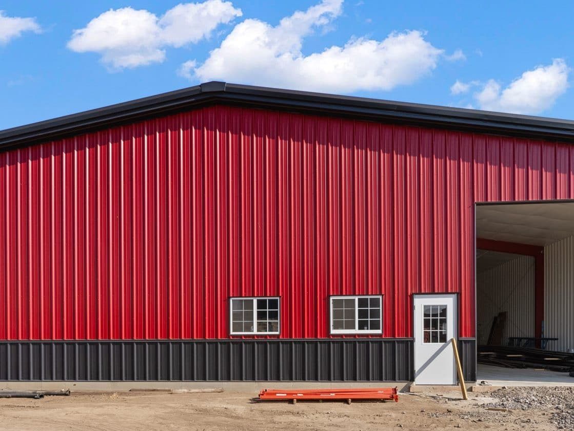 Red steel building with black wainscot, two windows, a walk door and a large open overhead door