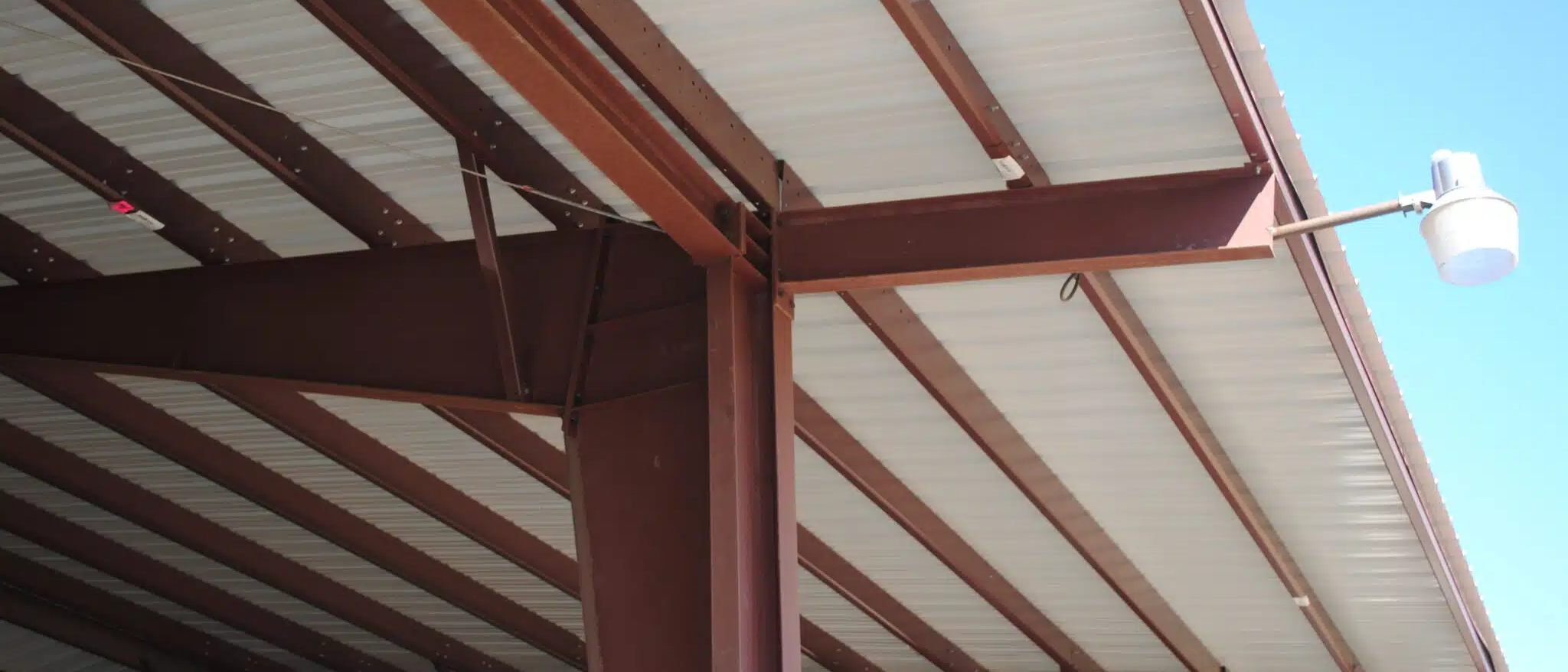 Close-up of red iron rafters and purlins under a metal roof at the eave of a steel building